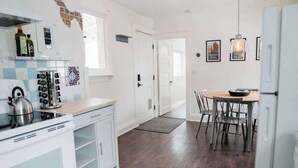 A modern kitchen with white cabinetry, a gas stove, and a coffee machine. There is a dining area with a wooden table and chairs.