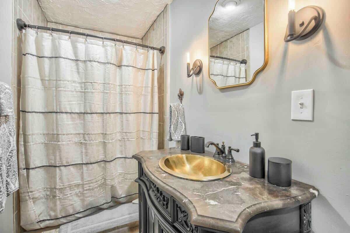 A bathroom with a marble sink, a gold-colored basin, a towel rack, a mirror with a gold frame, and a wall-mounted light fixture.