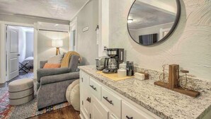 A living room with a gray sofa, a coffee machine, and a round mirror on the wall. - Miners Escape! Timeless District Cozy Haven (Colorado Springs)