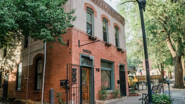 A brick building with a green door and windows, a street lamp, and a sidewalk with plants. - Miners Escape! Timeless District Cozy Haven (Colorado Springs)