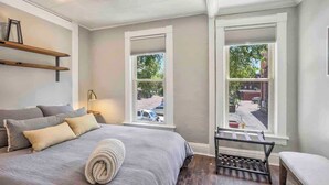 A bedroom with a bed, two windows, a bench, and a shelf. - Miners Escape! Timeless District Cozy Haven (Colorado Springs)