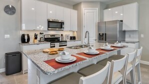 A modern kitchen with white cabinets, a granite countertop, stainless steel appliances, and a dining area with white chairs.