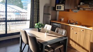 Eine moderne Küche mit Mikrowelle, Kühlschrank und Geschirrspüler. Ein Esstisch mit Stühlen und ein Blumentopf sind ebenfalls vorhanden.