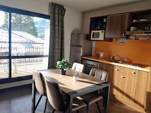 Cocina moderna con microondas, refrigerador y lavavajillas. Cuenta con una mesa de comedor, sillas y una planta en maceta.