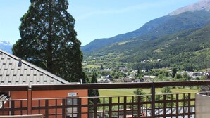 A balcony with a view of a village, mountains, and a tall tree. - 1st floor, swimming pool, hammam, terrace, parking, tv, 27m ², Pra Loup (Jausiers)
