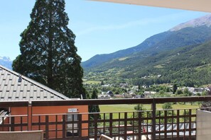 A balcony with a view of a village, mountains, and a tall tree. - 1st floor, swimming pool, hammam, terrace, parking, tv, 27m², Pra Loup (Jausiers)