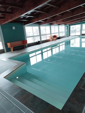 Una piscina interna con acqua limpida, panche lungo il bordo e ampie finestre.