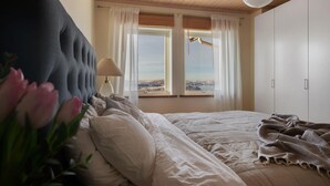 Ein Schlafzimmer mit einem großen Bett, Meerblick durch zwei Fenster und einer Holzbalkendecke.