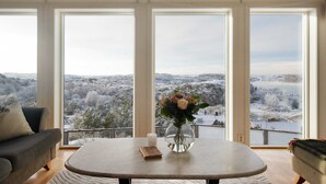 Ein modernes Wohnzimmer mit einem großen Fenster, einem runden Tisch, einer Blumenvase und einem Buch.
