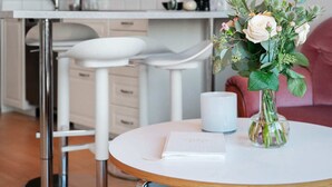 A modern kitchen with white cabinets, a stainless steel range hood, and a round dining table with a vase of flowers. - Sea-View Anexet in Fjällbacka by AJF Dream Living (Fjällbacka)
