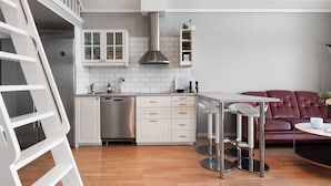 A modern kitchen with white cabinets, stainless steel appliances, and a dining area with a red sofa and a small round table. - Sea-View Anexet in Fjällbacka by AJF Dream Living (Fjällbacka)