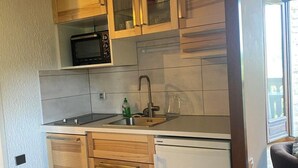 Una cocina compacta con armarios de madera, microondas, fregadero y lavavajillas.