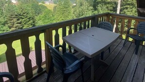 Una terraza de madera con una mesa y sillas, con vistas a un paisaje pintoresco de árboles y colinas.