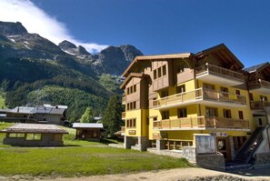Um hotel de vários andares com varandas, uma escadaria de pedra e montanhas ao fundo.