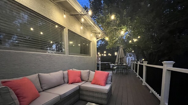 Terraza exterior con zona de estar acolchada, una mesa de centro de vidrio y luces colgantes.