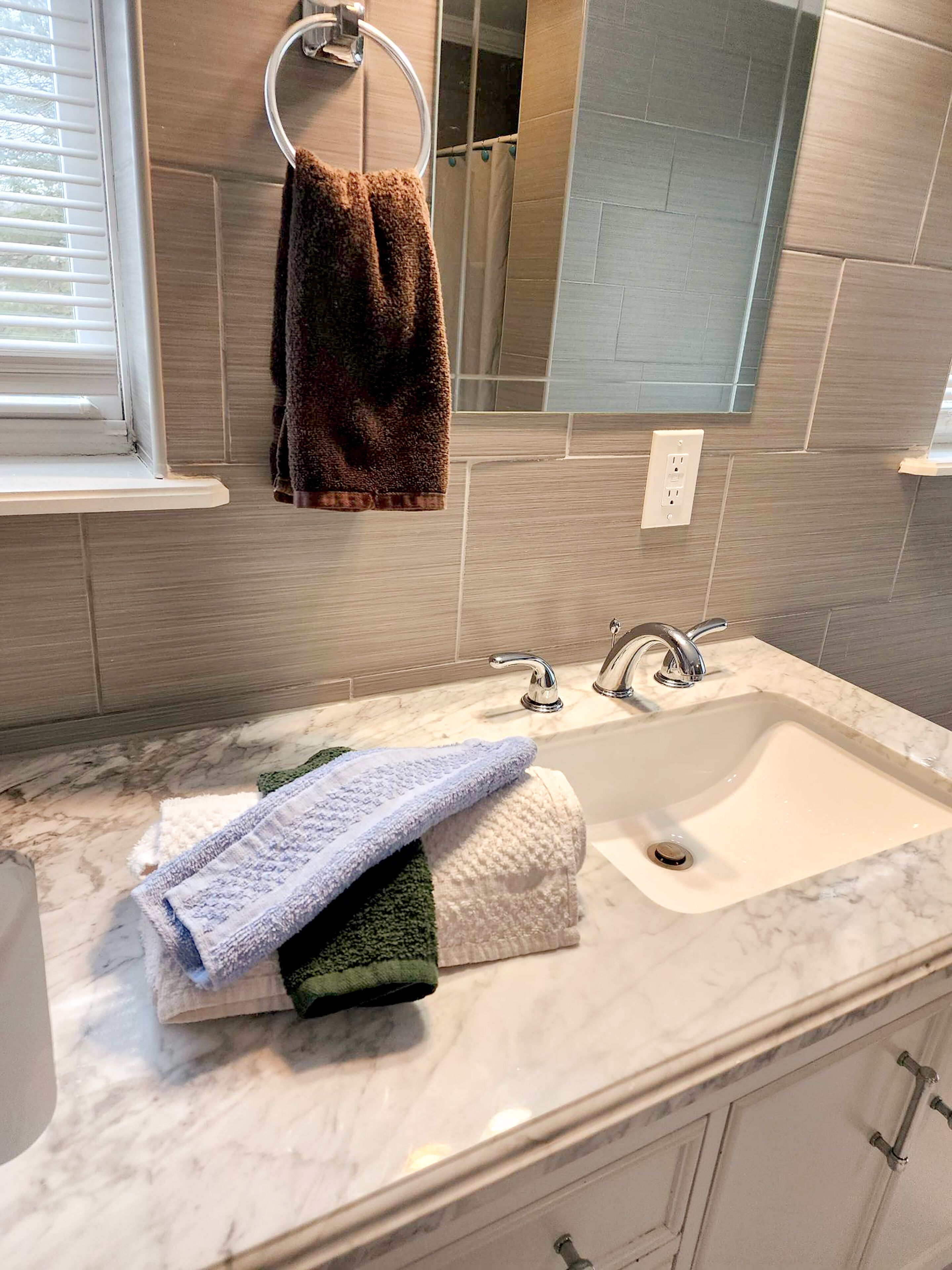 A bathroom with a marble sink, two faucets, and a towel rack with a brown towel.