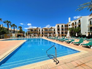 Une piscine avec des chaises longues et, au fond, un bâtiment doté de balcons.