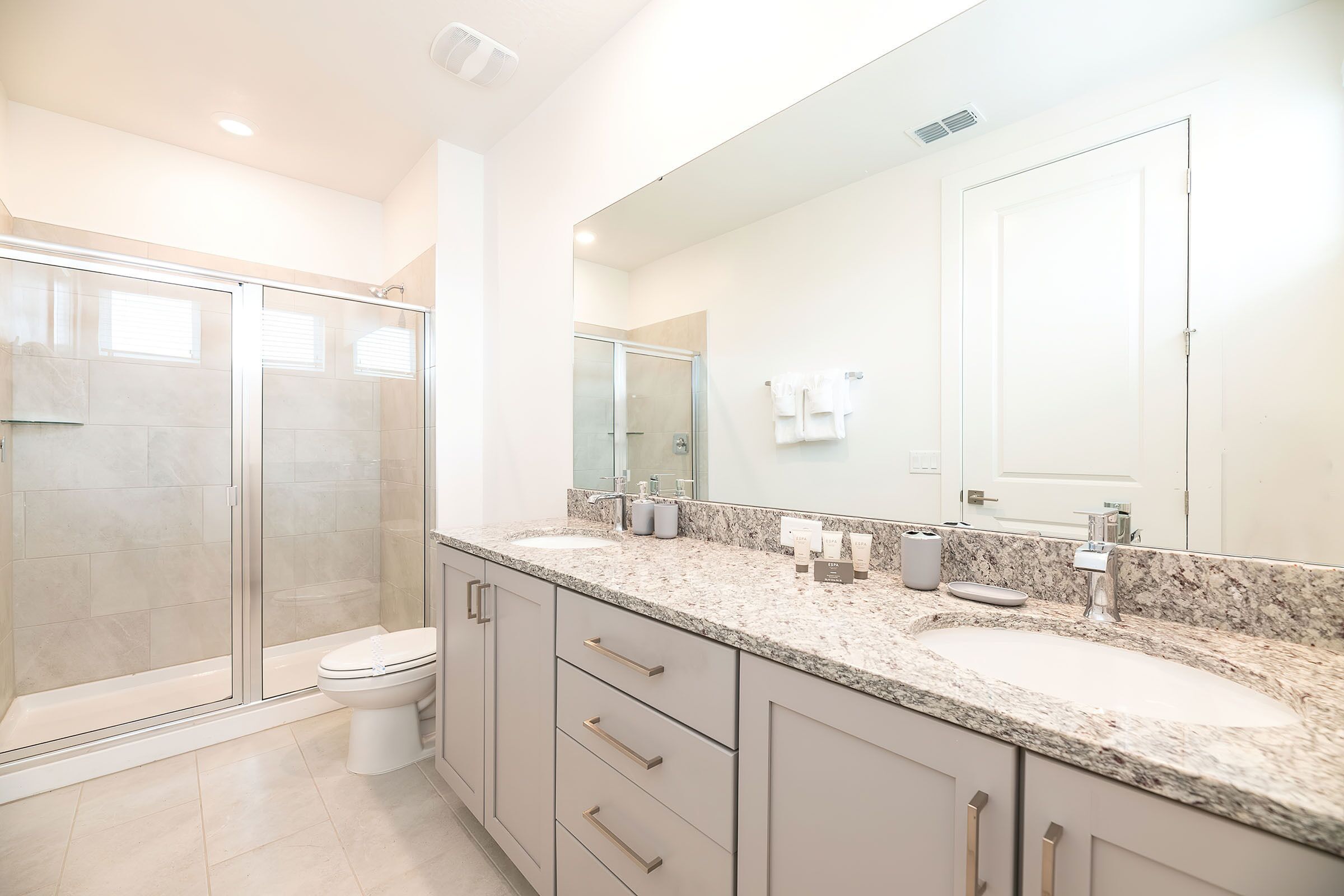 A modern bathroom with a glass-enclosed shower, a double sink vanity, and a large mirror.