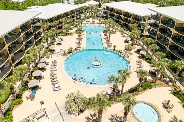 A hotel with a central swimming pool surrounded by sun loungers and palm trees.
