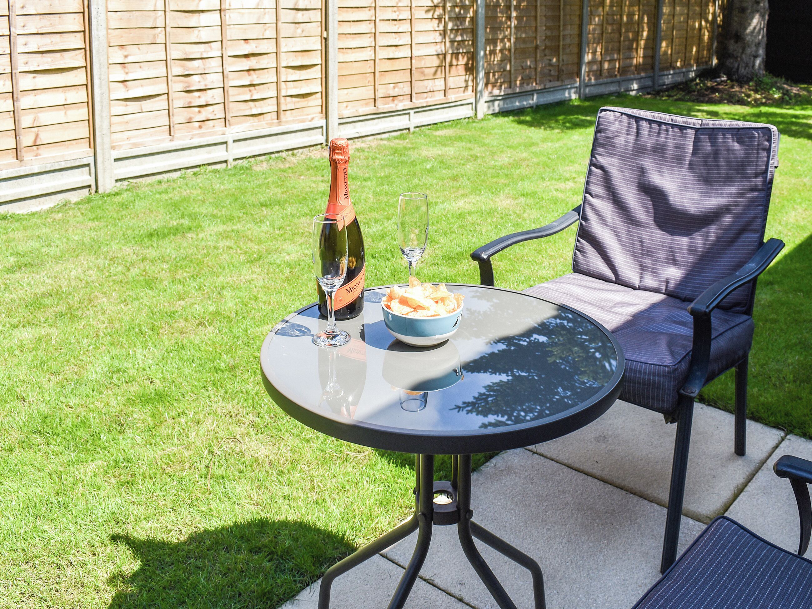 Une terrasse avec une table ronde, une chaise, une bouteille de champagne et un bol de collations.