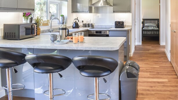 Uma cozinha moderna com ilha central, banquetas, eletrodomésticos de aço inoxidável e vista para um quarto.