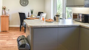 Uma cozinha moderna com uma ilha central, uma área de refeições com cadeiras, um relógio na parede e vista para o verde lá fora.