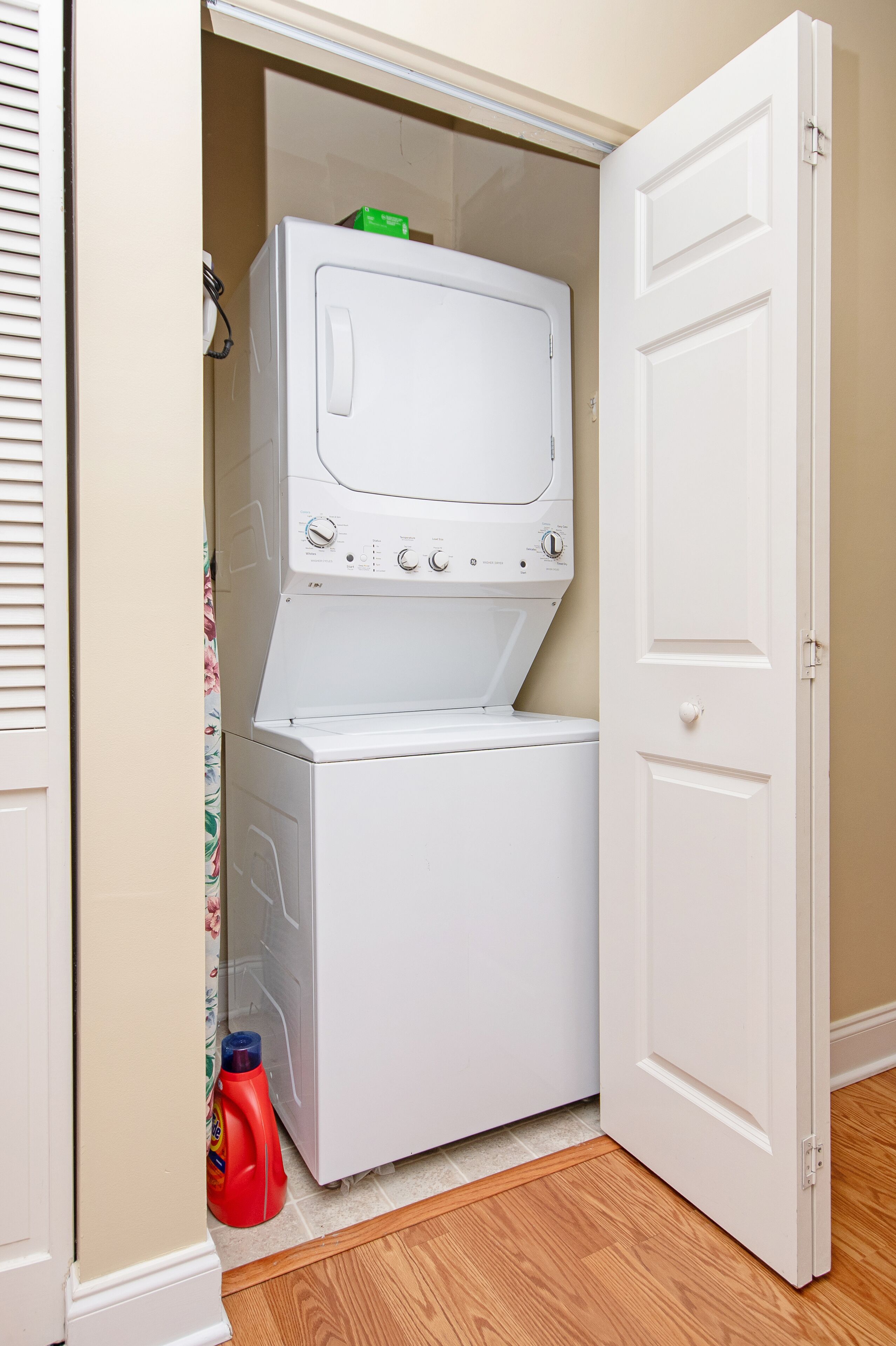 Une buanderie équipée d’un lave-linge et d’un sèche-linge à chargement frontal, d’une bouteille de lessive rouge et d’un plancher en bois.