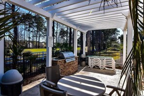 A covered patio with a grill, outdoor seating, and a view of a sports field. - Relaxing First Floor Condo on Golf Course with Pool (Myrtle Beach)