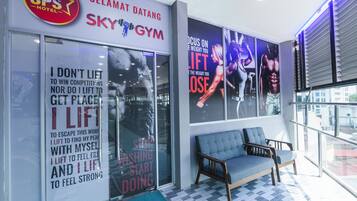 Un gimnasio con carteles motivacionales, una zona de recepción con un sofá azul y vistas a la ciudad a través de amplias ventanas.