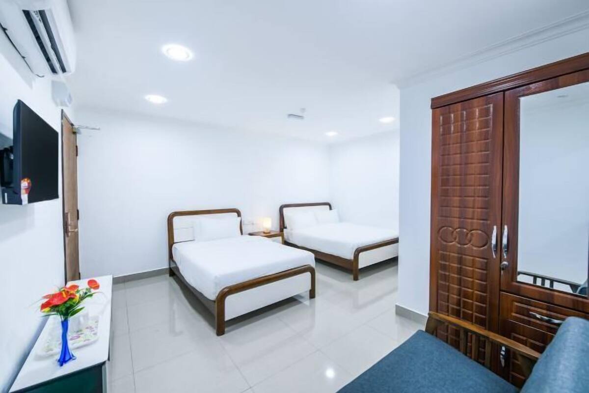 A hotel room with two beds, a TV, a desk with a vase of flowers, and a wardrobe.