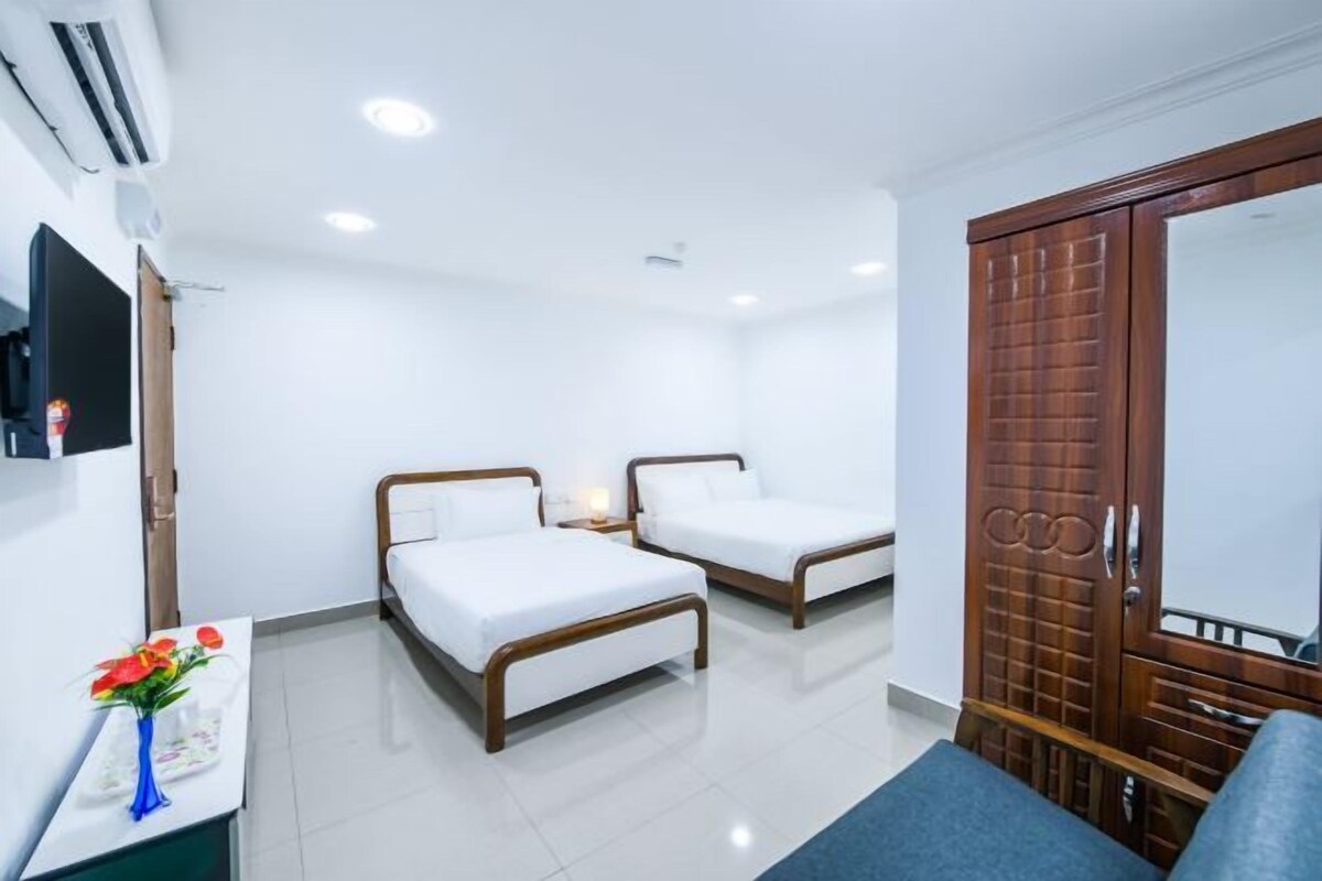 Habitación de hotel con dos camas, televisor, escritorio con un florero y armario.