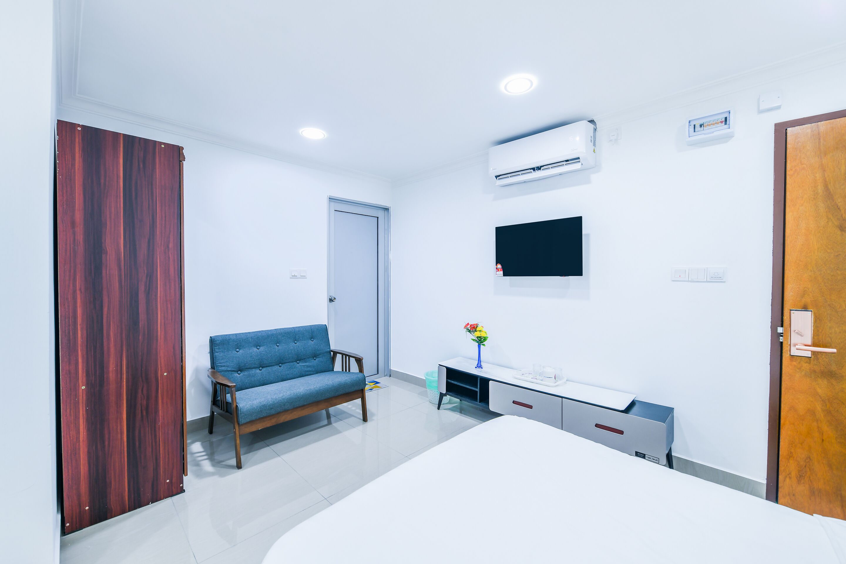 Habitación de hotel con cama, escritorio, silla, unidad de aire acondicionado, televisión y puerta de madera.
