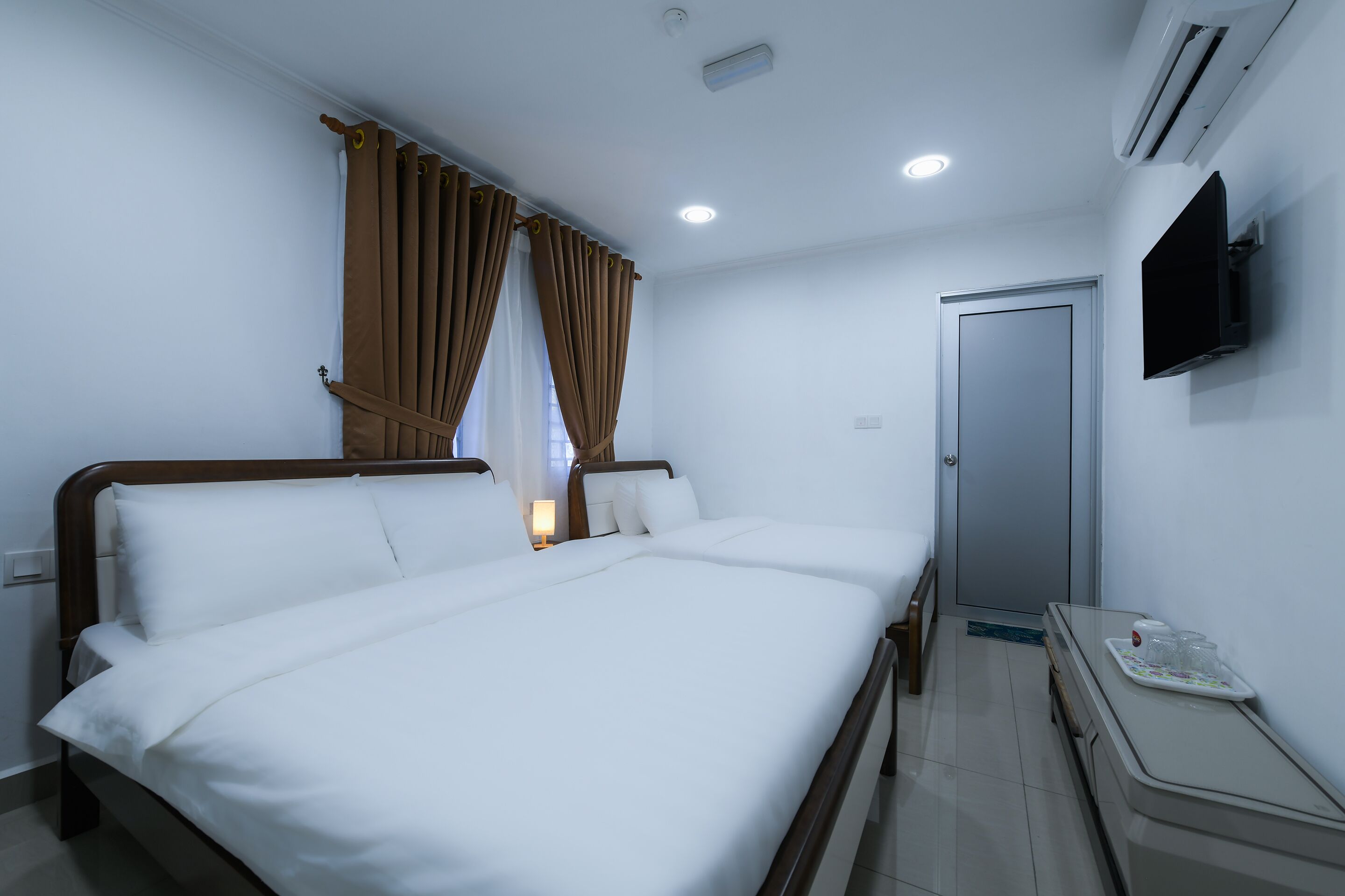 A hotel room with a bed, curtains, a TV, and a door.