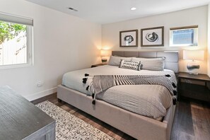 Une chambre à coucher moderne avec un grand lit, des tables de chevet, une petite table et des œuvres d’art accrochées au mur.