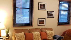 Una sala de estar con un sofá de cuero marrón, un tapete estampado y tres cuadros en la pared.