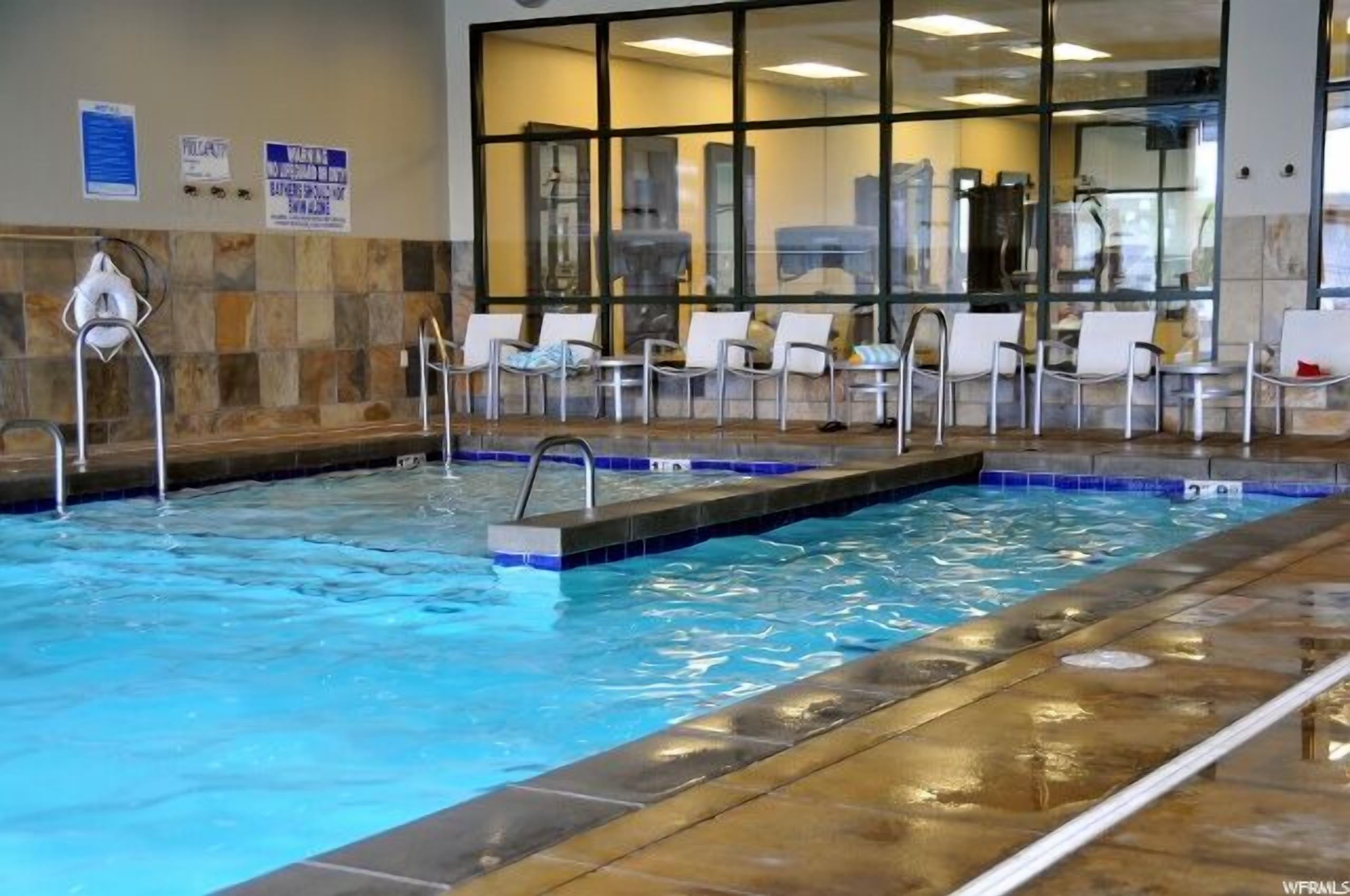 A swimming pool with lounge chairs and a glass wall.