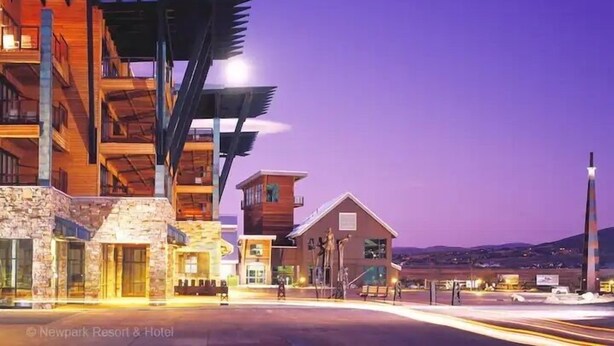 Un hotel moderno con fachada de piedra, varios balcones y una estructura metálica destacada.