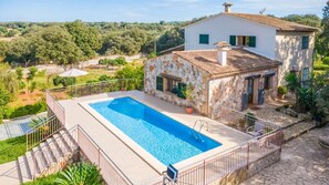 A villa with a swimming pool, stone walls, and a view of the surrounding landscape.