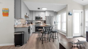Eine moderne Küche mit grauen Schränken, einem Edelstahlkühlschrank, einer Mikrowelle und einer Holz Arbeitsplatte. Vier Hocker stehen um einen zentralen Tisch.