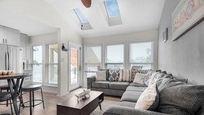 Ein modernes Wohnzimmer mit einem grauen Sofa, einem dunklen Couchtisch und einem Essbereich mit Tisch und Stühlen.