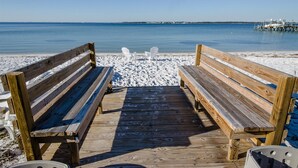 Eine Holzsteg führt zu einem Sandstrand, mit zwei Holzbänken, die zum Wasser ausgerichtet sind.