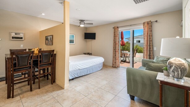 Habitación de hotel con cama, escritorio con sillas, televisión y balcón con mobiliario exterior.