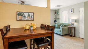 Un comedor con una mesa y sillas de madera, una pequeña planta en maceta y un cuadro con cactus en la pared.