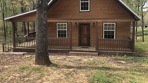A wooden cabin with a porch, a front door, and two windows.
