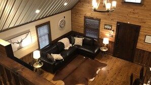 A cozy cabin interior with a black leather sofa, a wooden ceiling, a large clock, and a rustic ambiance.