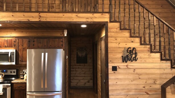 A spacious kitchen with a stainless steel refrigerator, wooden cabinets, and a microwave. A staircase leads to a loft area with a wooden railing.