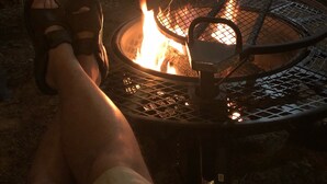 A person relaxing by a fire pit with a chair and a table nearby.