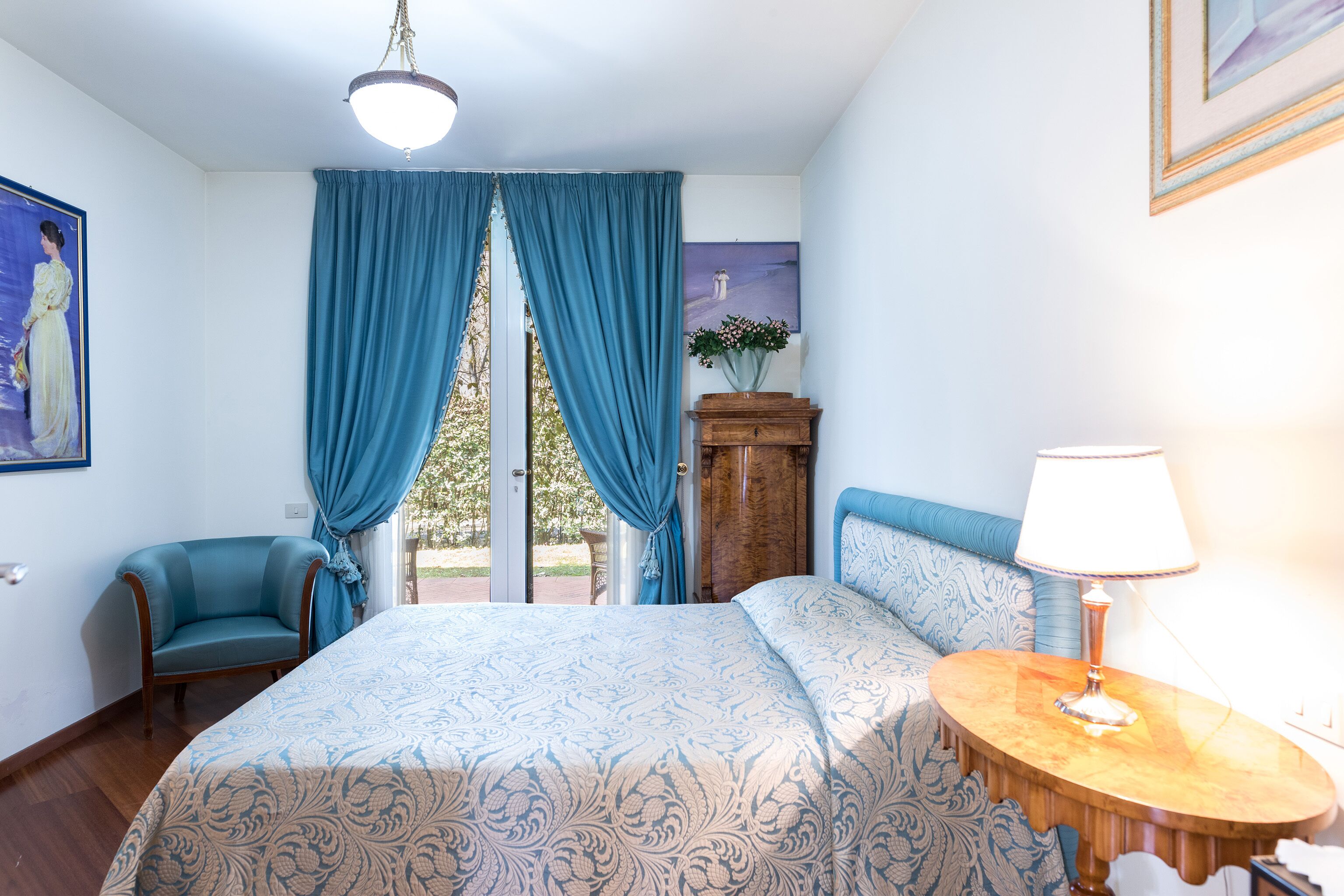 A bedroom with a large bed, a chair, a wooden cabinet, and a lamp.
