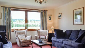 A living room with a sofa, armchairs, a coffee table, and a view of a green landscape through large windows. - 4 bedroom accommodation in Spittalfield, nr Dunkeld (Spittalfield, nr Dunkeld)