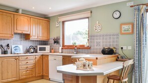 A kitchen with wooden cabinets, a microwave, a sink, and a dining area with a chair. - 4 bedroom accommodation in Spittalfield, nr Dunkeld (Spittalfield, nr Dunkeld)